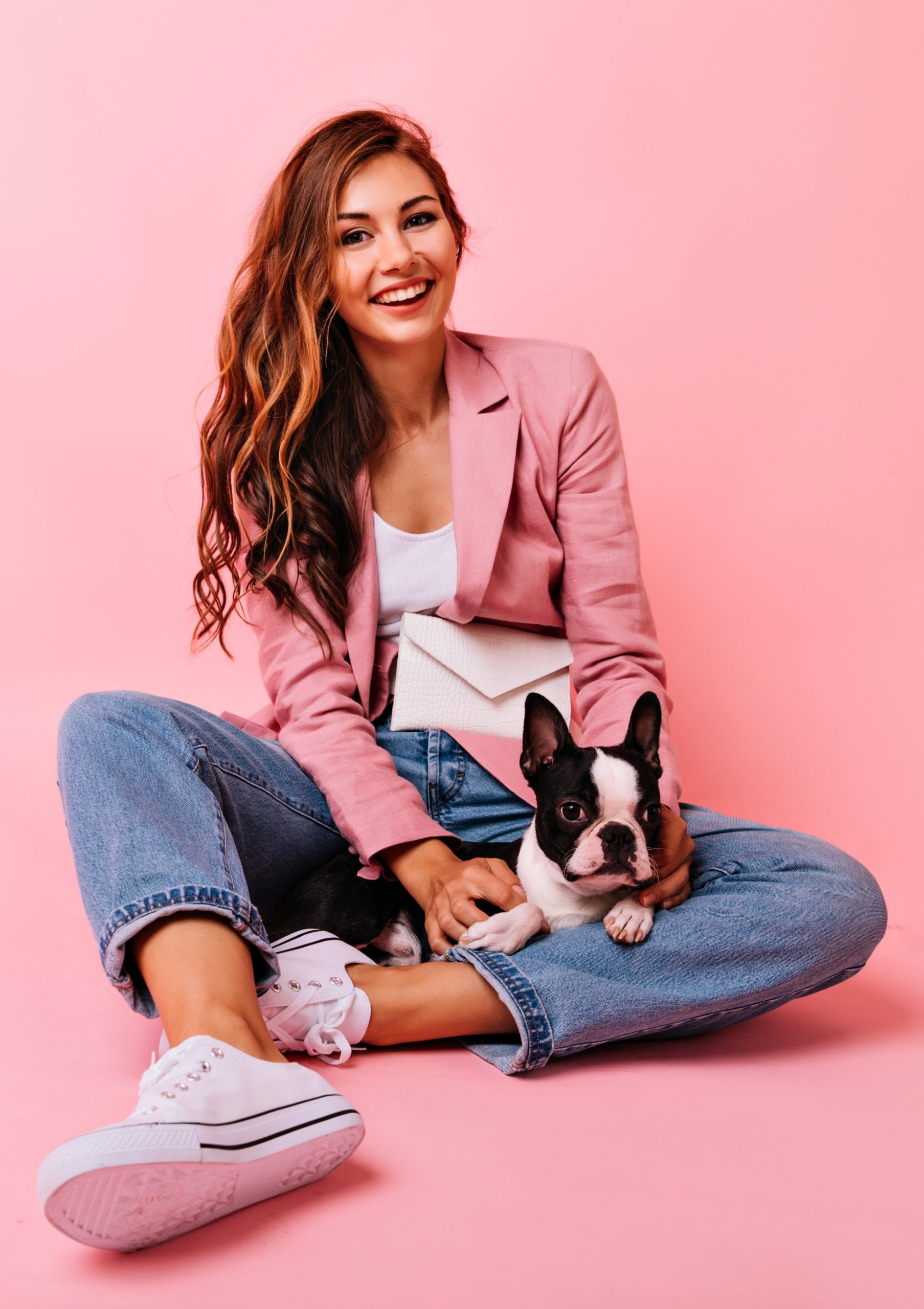 Enchanting girl in white sport shoes posing with dog. Laughing winsome woman sitting on the floor with cute bulldog puppy.